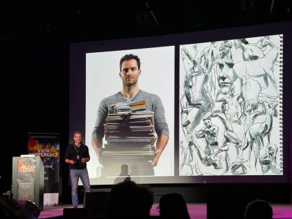 Scott Eaton on stage at the View Conference, showing himself holding a stack of sketchbooks.